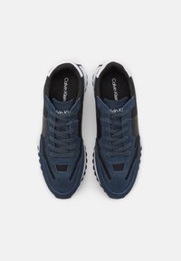 Sneaker blu navy in suede e mesh con dettagli neri, dotati di suola in gomma e design con lacci. Logo Calvin Klein visibile.