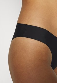 Black thong underwear with a smooth, matte texture and a seamless waistband, displayed against a light background.