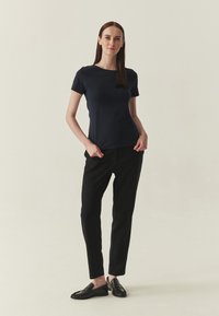 T-shirt bleu marine à manches courtes avec un col rond, associé à un pantalon noir fuselé et des chaussures noires à enfiler avec une texture à volants.