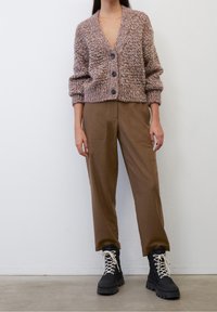 Tlustý pletený cardigan v růžově béžové barvě se třemi knoflíky, doplněný hnědými kalhotami a černými šněrovacími botami s tlustou podrážkou.