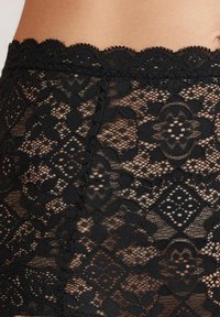 Svart spetstyg med blommiga och geometriska mönster, med en vågig midja som framhäver intrikata detaljer och textur.