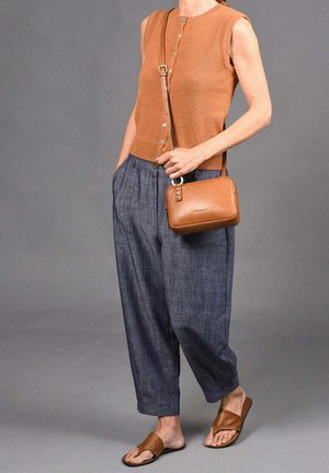 Brown sleeveless top with buttons, loose blue pants, and brown slide sandals. Small brown crossbody bag with a zipper and strap.