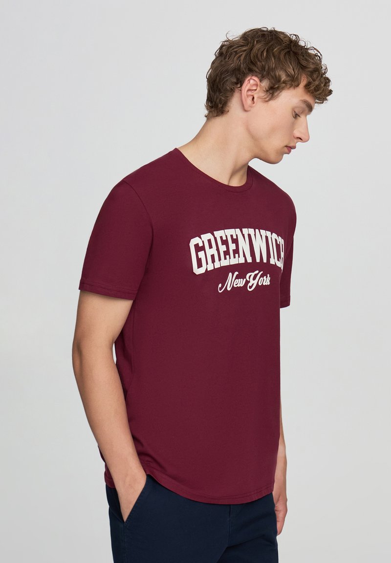T-shirt bordeaux a maniche corte con la scritta "GREENWICH New York" in lettering bianco. Collo tondo, tessuto liscio, vestibilità comoda.