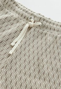 Korte broek in beige met een geometrisch patroon, een elastische tailleband en een trekkoord. Voorzien van zilverkleurige metalen oogjes en een zachte textuur.