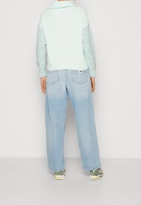 Hellblauer Strickpullover mit Kragen, kombiniert mit locker sitzenden hellen Denim-Jeans. Das Outfit umfasst lässige Sneakers und zeichnet sich durch eine entspannte Passform aus.