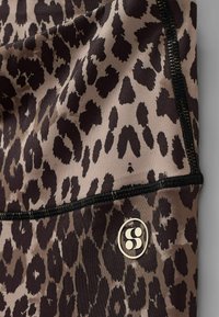 Leopardi mustriga retuusid pruunide ja mustade toonidega. Asuvad sujuva, veniva kanga peal, mustade õmblustega ja ümmarguse kuldse logo detailiga.