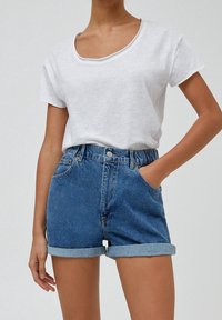 Camiseta blanca de manga corta con cuello redondo combinada con pantalones cortos de mezclilla de tiro alto en azul, con puños enrollados y bolsillos laterales.