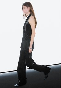 Black velvet two-piece outfit featuring a sleeveless top and wide-leg pants, complemented by a silver bangle and pointed black shoes.