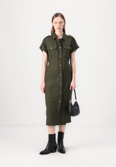 Robe olive verte à manches courtes, avec deux poches poitrine et des accessoires en argent. Assortie à des bottines noires et un petit sac à main.