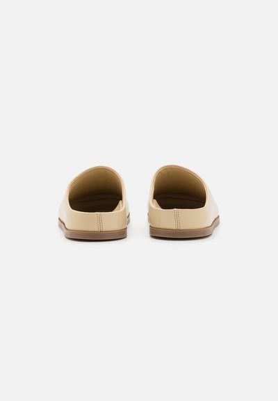 Chaussures beiges à enfiler avec ouvertures incurvées, en matériau synthétique lisse, au design minimaliste, et une semelle en caoutchouc brun. Détails de couture soignés.
