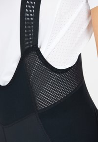 Schwarzes Sportoberteil mit Mesh-Details und verstellbaren schwarzen Trägern. Verfügt über ein strukturiertes Paneel und glattes Material. Leichtes Design.