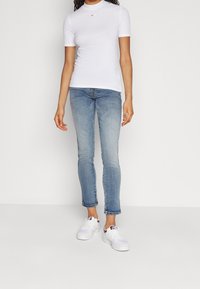 Biała dopasowana koszulka z okrągłym dekoltem, w połączeniu z jasnoniebieskimi rurkami i białymi trampkami z burgundowymi akcentami. Prosty design, casualowy wygląd.