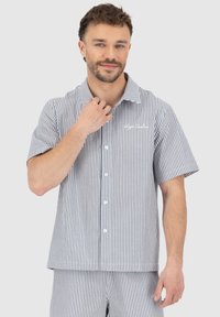Short-sleeve, collared shirt in blue and white vertical stripes, featuring front buttons and chest logo, made from lightweight fabric.