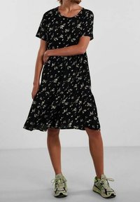 Černé květinové šaty s krátkými rukávy, nařaseným pasem a splývavou sukní. Nosené s zelenošedými teniskami.