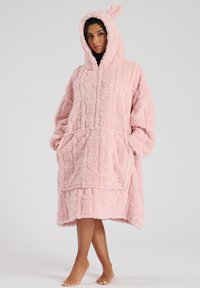 Robe oversize rosa con un tessuto dalla texture particolare, dotata di cappuccio con orecchie, tasche frontali e un design che arriva fino al ginocchio. Materiale morbido e peloso.