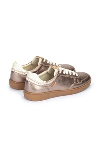 Zapatillas metálicas bronce con detalles en blanco, que cuentan con una textura suave, puntera redonda y suela de goma. Costuras decorativas en el talón.