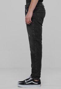 Jeans ajustados negros con un acabado desgastado, con una cintura de altura media y textura de denim estándar. Combinados con zapatillas negras y blancas.