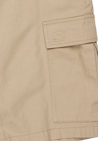 Shorts cargo beige en tissu léger, avec un motif texturé, poche latérale avec rabat et détails de couture renforcée.