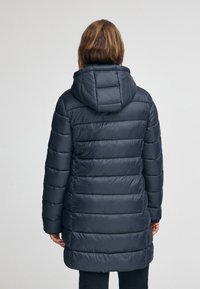 Marinblå puffjacka med huva, med kviltade sektioner, slät yta och elastiska ärmslut. Jackan har en medellång design.