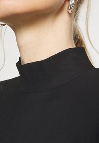 Svart polokragetröja med ribbat mönster och figurnära design. Närbild som fokuserar på halsringningen och den omgivande huden.