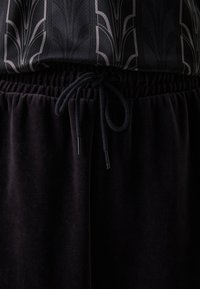 Sorte joggingbukser lavet af blødt stof, med en elastisk talje med snor og metalender, parret med en mønstret top.