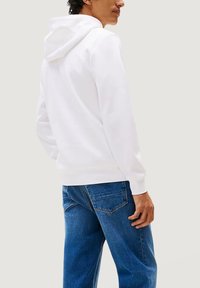 Felpa bianca con cappuccio realizzata in morbido misto cotone, con tasca a marsupio e polsini a costine, abbinata a jeans denim blu.