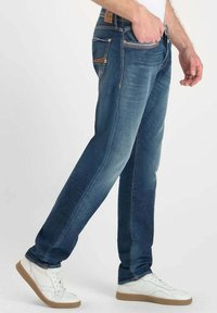 Jeans de mezclilla azul en corte recto, con bolsillos delanteros y traseros, un ligero desgaste y costuras de contraste. Combinados con zapatillas blancas.