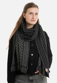 Zwarte en grijze sjaal met een patroon van zacht materiaal, met geometrische ontwerpen. Om de nek gewikkeld, voegt textuur toe aan een zwarte outfit.