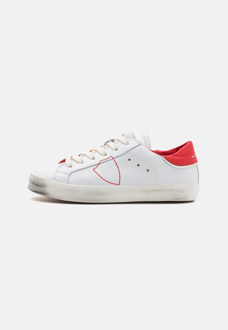 Zapatilla blanca con acentos rojos, material de cuero, punta redonda, diseño cosido destacado y suela de goma clara con ligero desgaste.