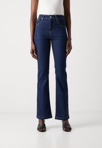 Mørkeblå jeans med vidde, laget av denim, med kontraststing og høy midje. De har frontlommer og glidelås.