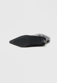 Stivale alla caviglia in pelle nera con punta affusolata, design chiuso, texture liscia e un sobrio dettaglio a fibbia. Suola in gomma piatta e striata.