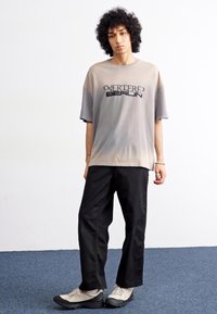 Oversized gray t-shirt with black lettering, paired with loose black pants and gray sneakers, set against a plain background.