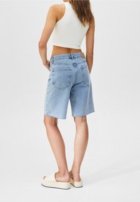 Shorts en denim bleu clair avec ourlet effiloché, cinq poches et taille haute. Associés à un crop top blanc côtelé et des sandales compensées beige.