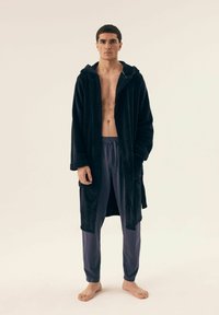 Czarny pluszowy szlafrok z kapturem, z otwartym przodem i długimi rękawami, w połączeniu z miękkimi fioletowymi spodniami do spania, na neutralnym tle.