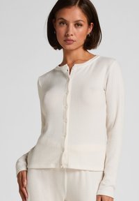 Ribbed, cream-colored knit cardigan with long sleeves and a rounded neckline, featuring a row of six buttons down the front.