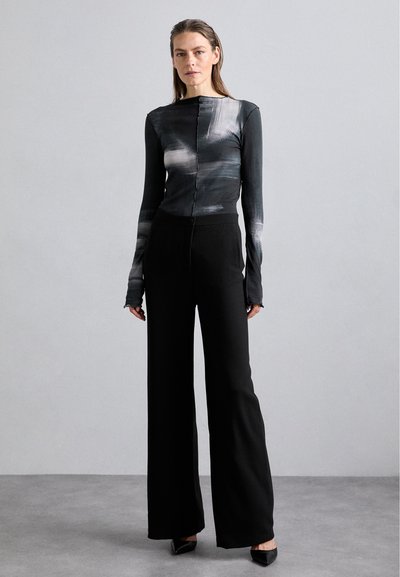 Black wide-leg pants paired with a long-sleeve top featuring a gray abstract pattern and button detail at the front. Fabric is smooth and fitted.