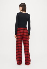 Sort langærmet top kombineret med rød og sort ternet brede bukser. Outfit'et har en elastisk talje og en glat, blød stoftekstur.