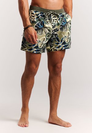 Shorts de bain pour hommes de couleur verte avec un motif de feuilles tropicales en bleu marine, blanc et noir. Dotés d'une ceinture élastique et d'un cordon de serrage.