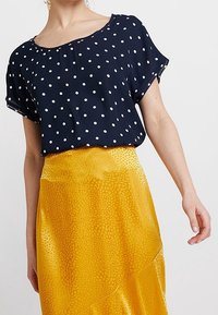 Námořnická polka dot blůza s krátkými rukávy v kombinaci s jasně žlutou, strukturovanou, asymetrickou sukní se vzorem leopardího tisku.