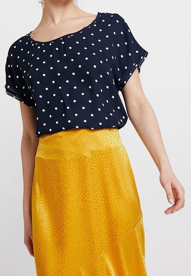 Námořnická polka dot blůza s krátkými rukávy v kombinaci s jasně žlutou, strukturovanou, asymetrickou sukní se vzorem leopardího tisku.