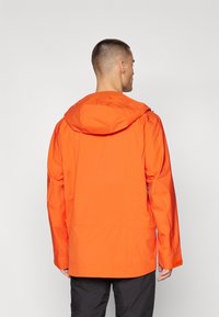 Nepremokavá oranžová bunda s kapucňou. Má dlhé rukávy, nastaviteľné manžety a dve bočné vrecká. Hladká textúra.