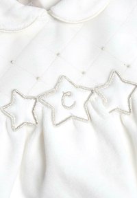 Tejido blanco acolchado con un cuello, que presenta tres estrellas bordadas en plata y una "c" decorativa en la estrella central. Superficie texturizada.