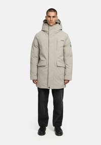 Gai pelēks spilvenveida parka ar augstu apkakli, lielām kabatām un kapuci. Dizains ir ar smalku zīmola atpazīstamību un taisnu siluetu.