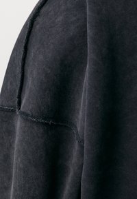 Schwarzer Sweatshirtstoff mit einer weichen Textur. Hat sichtbare Nähte und einen leicht ausgefransten Rand an der Schulternaht.