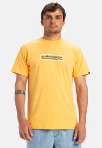 Yellow cotton t-shirt with a round neckline, featuring a black and white logo design across the chest, short sleeves, and a relaxed fit.
