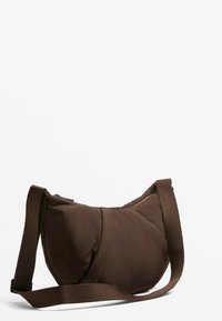 Hnědá prošívaná kabelka přes rameno s jemnou texturou, širokým popruhem a zakřiveným tvarem. Zapínání na zip s minimalistickými designovými detaily.