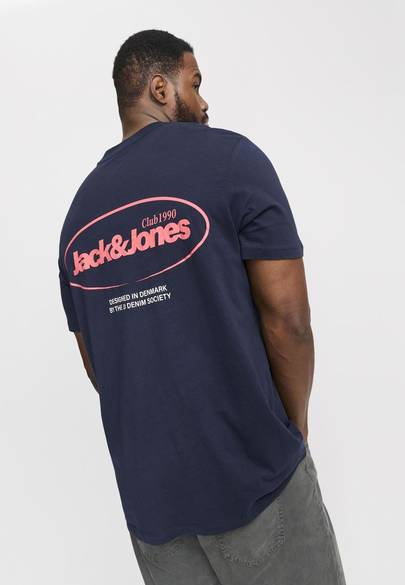 Marineblaues T-Shirt mit kurzen Ärmeln und pinkem, gedrucktem Logo "Jack & Jones Club1990" auf dem Rücken. Aus weichem Baumwollmaterial mit lässiger Passform.