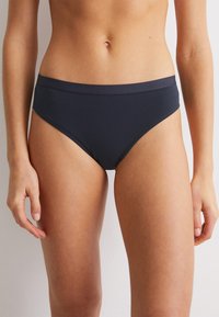 Mörkblå bomullshipsterunderkläder med en bred midjeband som har präglad branding, slät textur och en figurnära design.