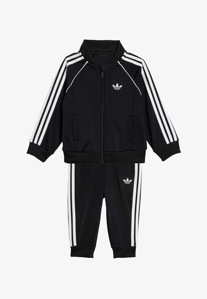 Juodas sportinis kostiumas, susidedantis iš užtrauktuku užsegamo džemperio su aukštu apykakliu ir baltomis juostelėmis, derančių kelnių, pagamintų iš lygaus audinio.