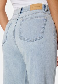 Lichtblauwe denim jeans met een hoge taille, voorzien van achterzakken en een tan leren label met "BUBBLEROOM" op de tailleband.